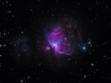 Photograph of a galaxy with gradients of pink, purple, blue, and white surrounded by scattered shining stars in outer space